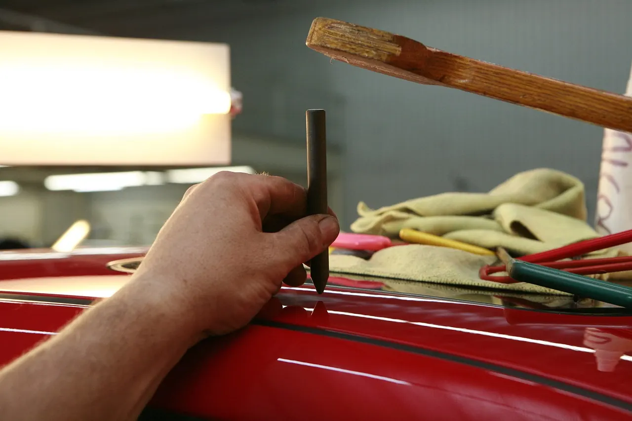 Hand using a pointed tool on the glossy red paint of a car body