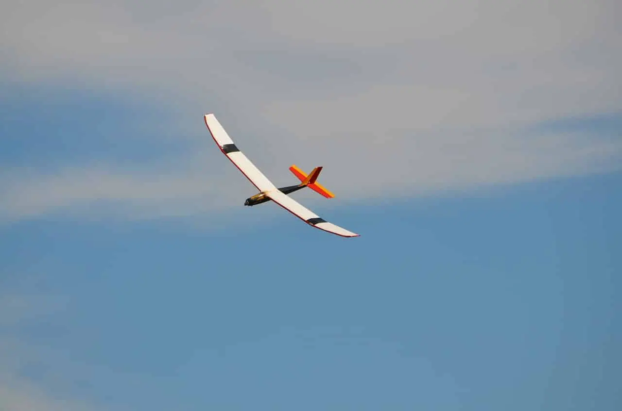 White RC glider with an orange tail flying against a blue sky