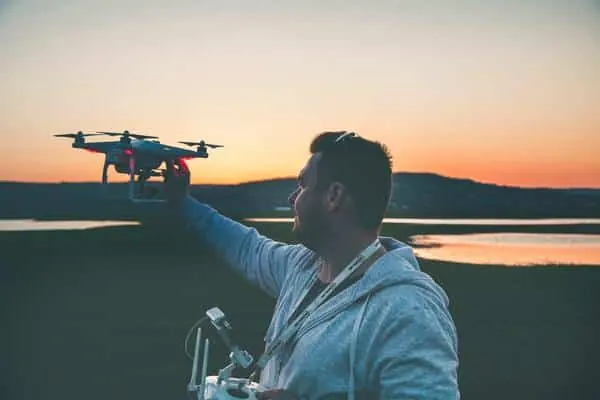 Man launching a white quadcopter from his hand at sunset beside a lake