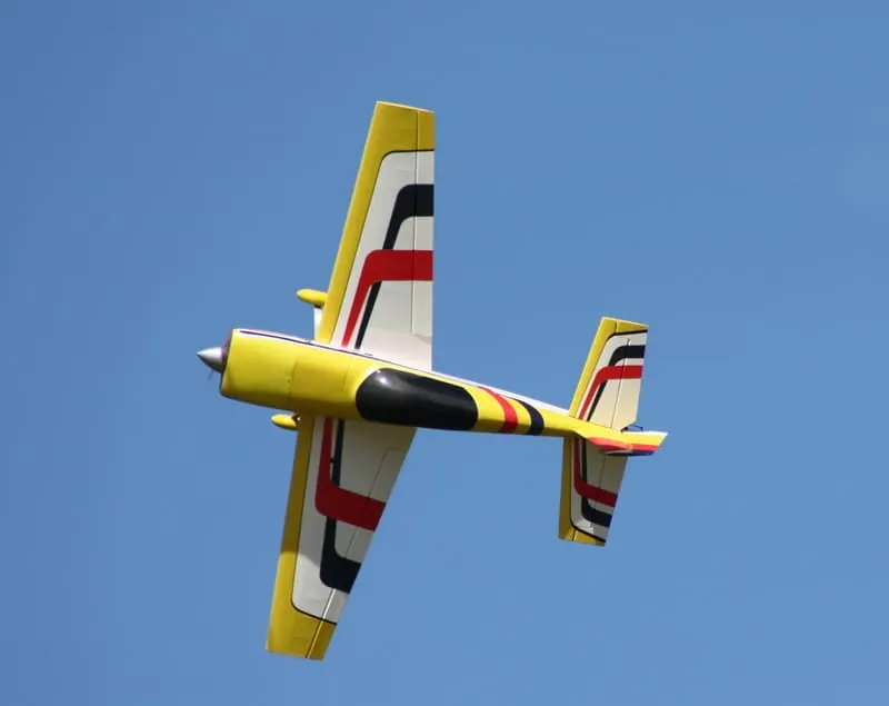 Yellow aerobatic RC plane flying against a blue sky