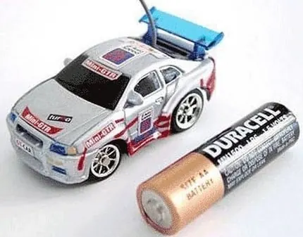 Tiny RC touring car with a rear wing next to an AA battery, showing its small size