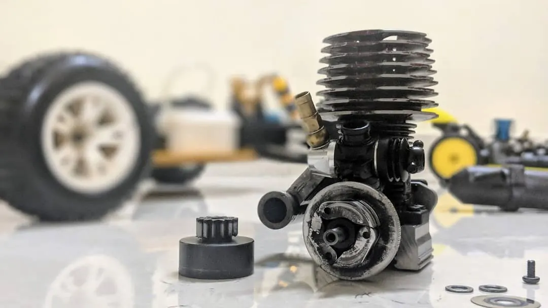 Nitro RC engine with its cooling head, next to an RC car wheel on a workbench