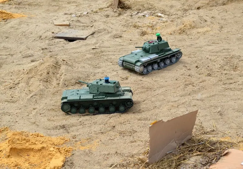 Two green RC tanks driving across a sandy battlefield course