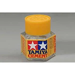 Hexagonal glass bottle of Tamiya Cement with an orange cap, on a gray background