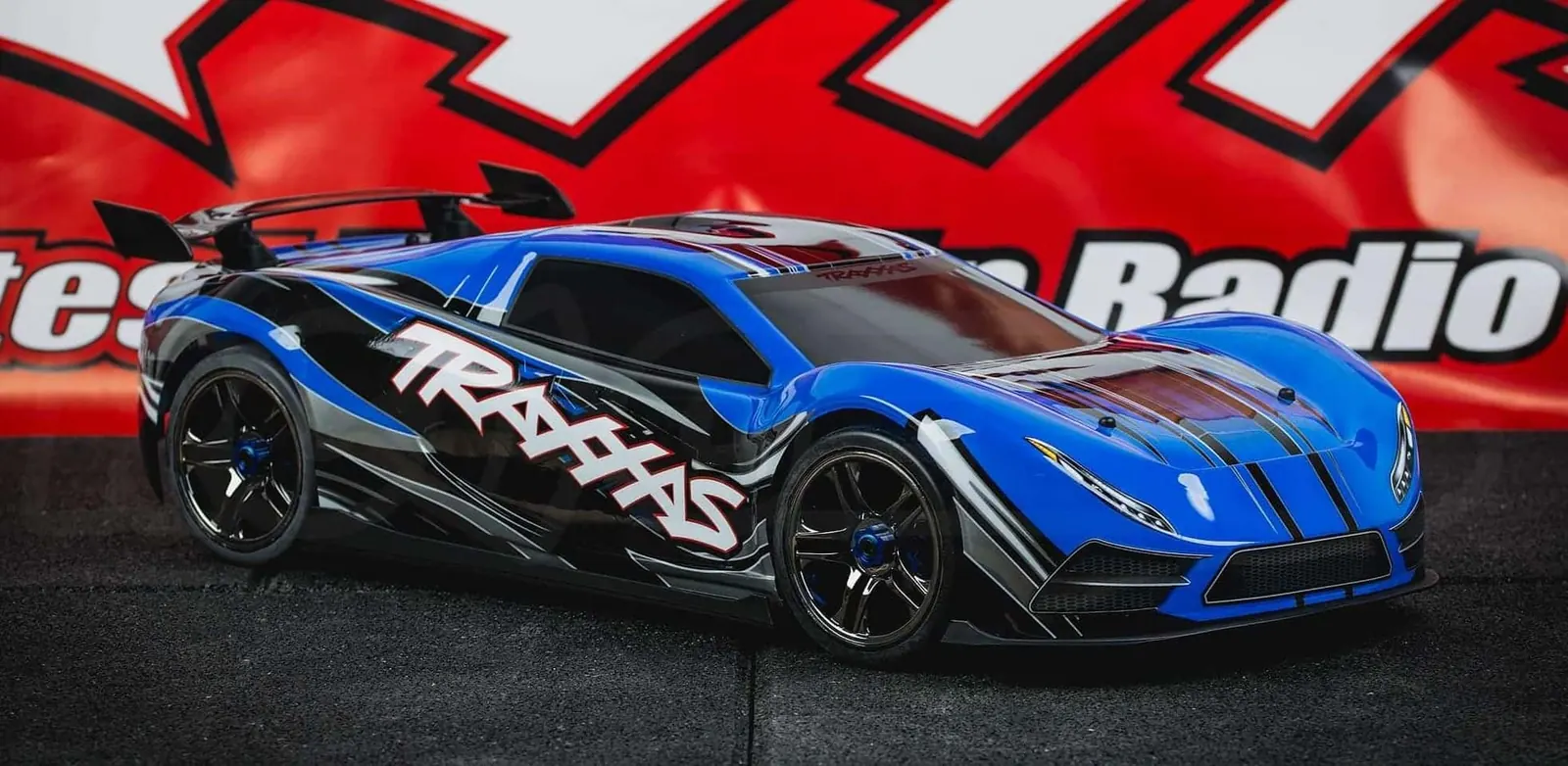 Blue Traxxas XO-1 in front of a red Traxxas banner